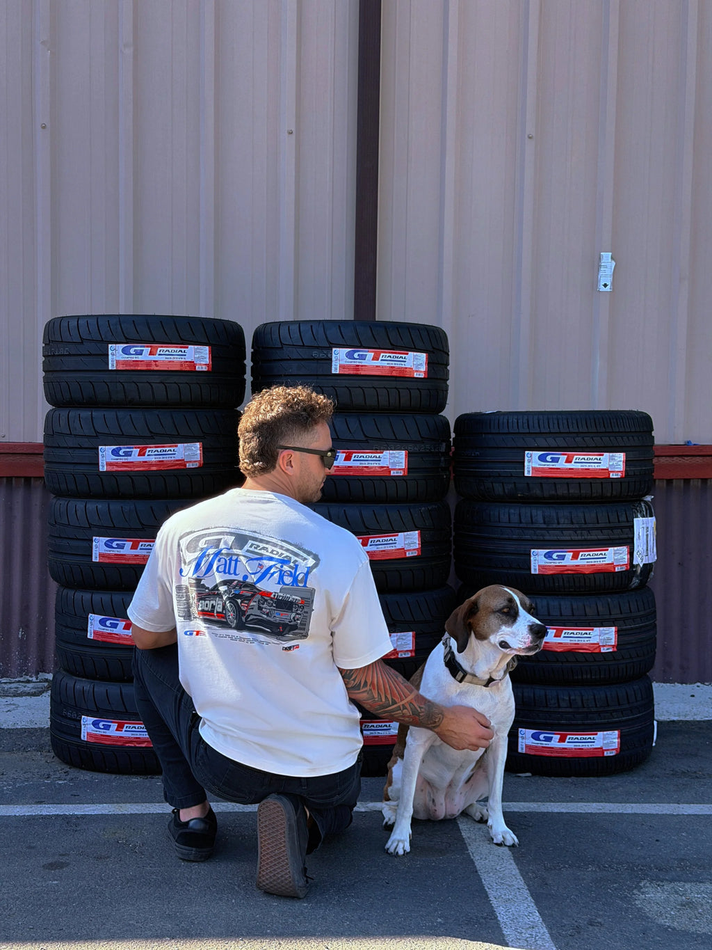 White tee with colorful car graphic on back, worn by person kneeling with a dog