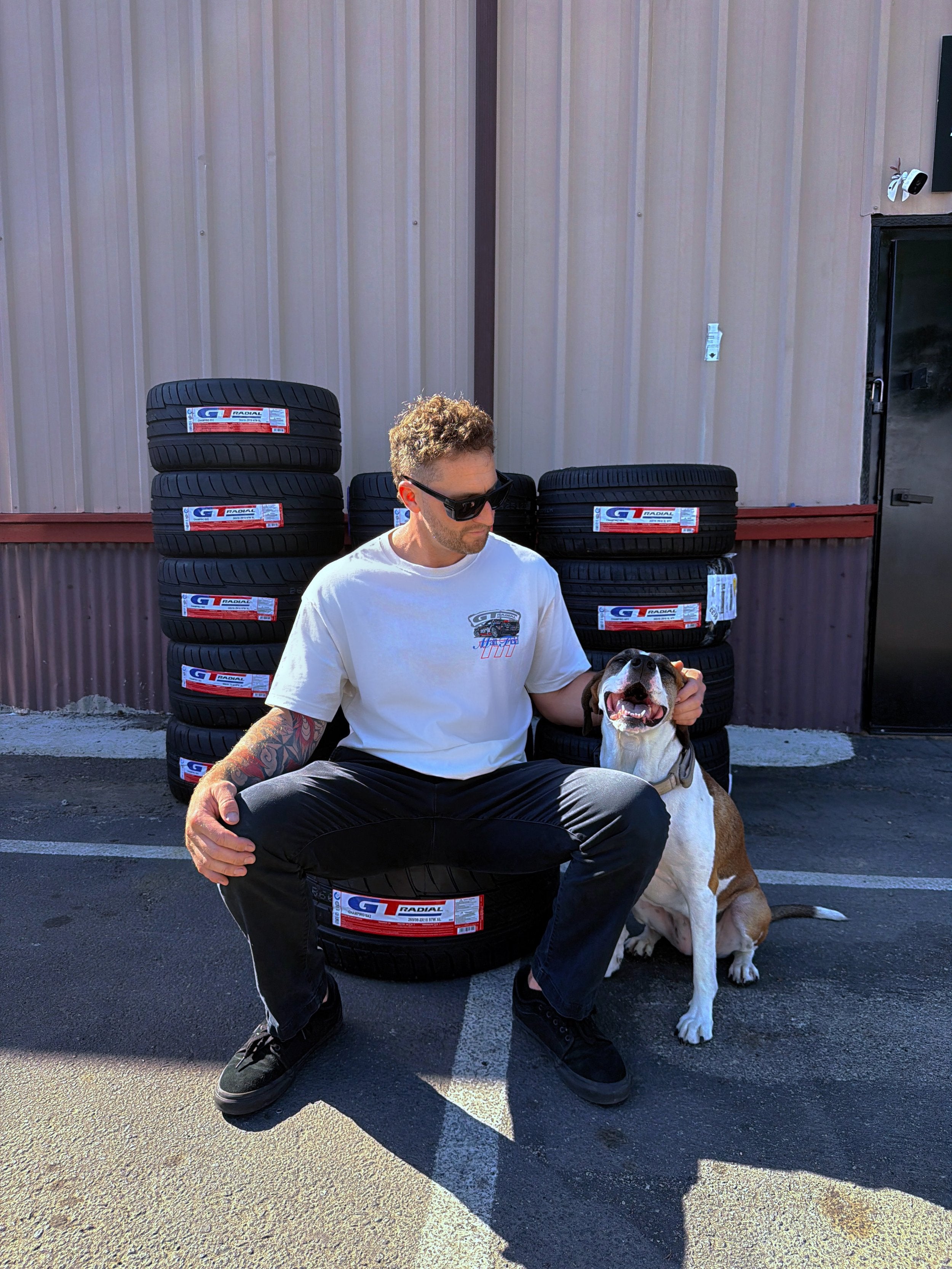 White T-shirt with small colorful race car graphic on chest, worn while kneeling with dog